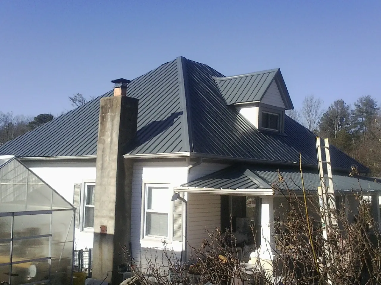 Dark blue standing seam metal roof on a white farmhouse with dormer — Slate & Tile Roof Repair by Roofing Brothers in Stonewall