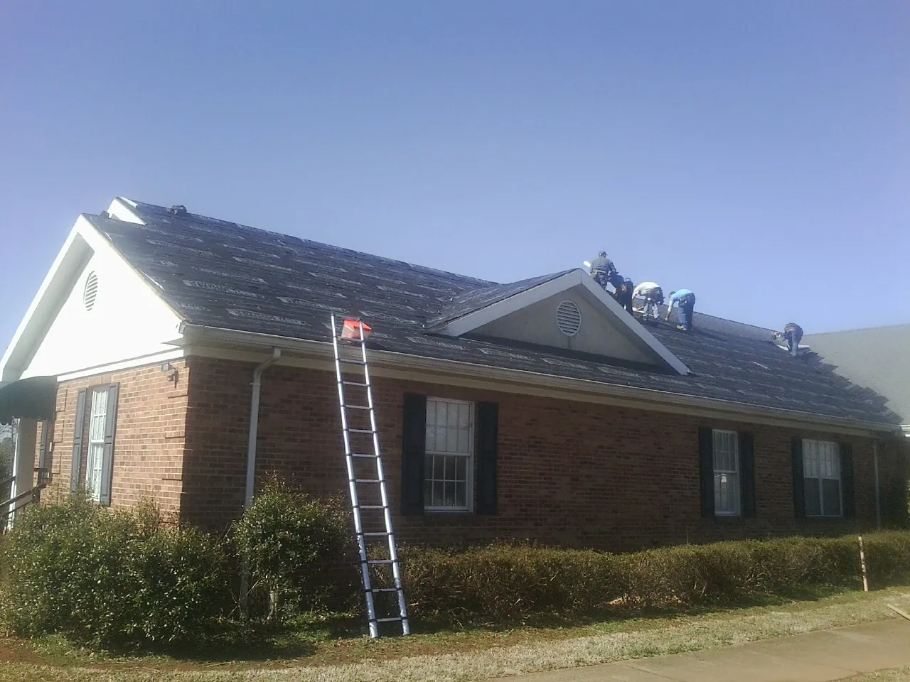 Crew tearing shingles off a brick ranch roof with a ladder set — Metal Roof Repair work by our crew in Stonewall