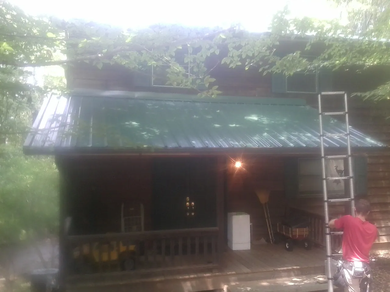 Worker on a ladder at the green porch roof of a wooded cabin in Stonewall