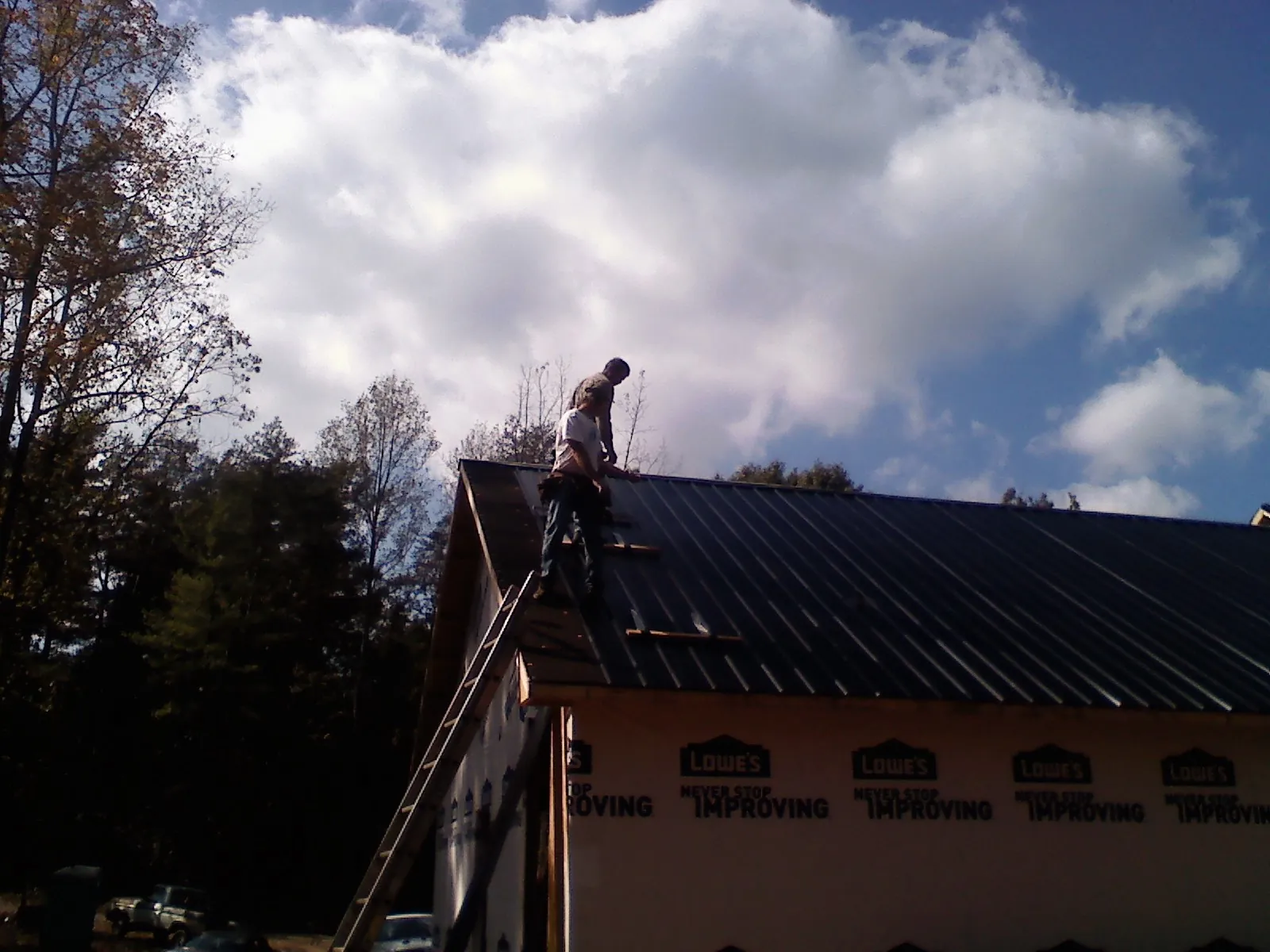Roofer fastening dark metal panels high against a cloudy sky, from a Roof Inspection job in Stonewall